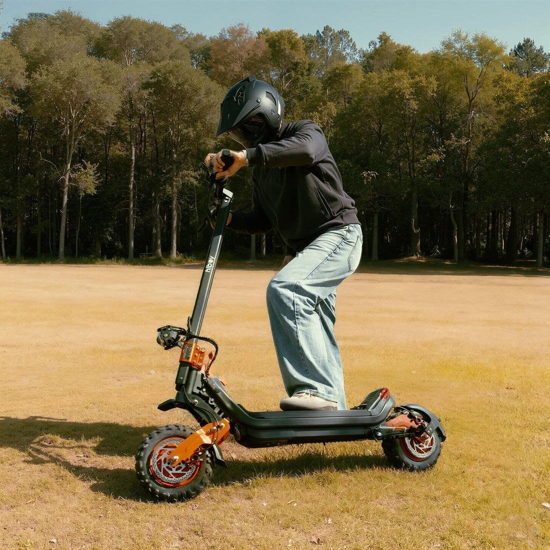 Person riding an off-road electric scooter in a grassy field with forest background