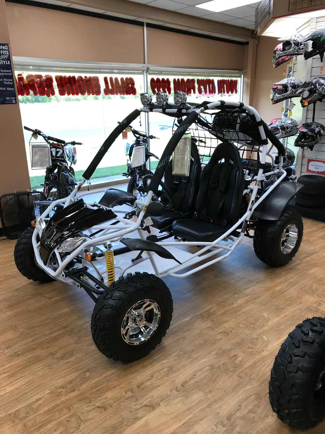 Large double seat go-kart with off-road tires and roll cage, displayed in showroom