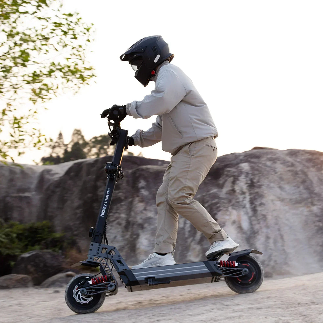 Person riding off-road electric scooter on rocky terrain wearing helmet and safety gear