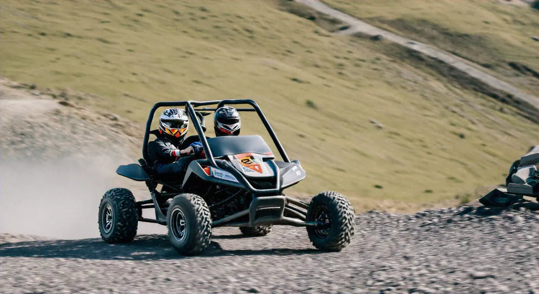 Two riders in helmets driving an off-road go-kart on a dirt trail outdoors