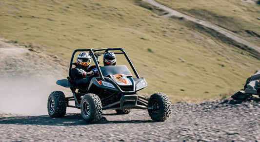 Two riders in helmets driving an off-road go-kart on a dirt trail outdoors