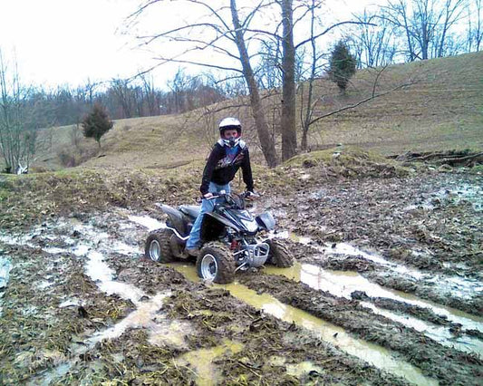 Rider on ATV navigating muddy off-road trail in a winter landscape