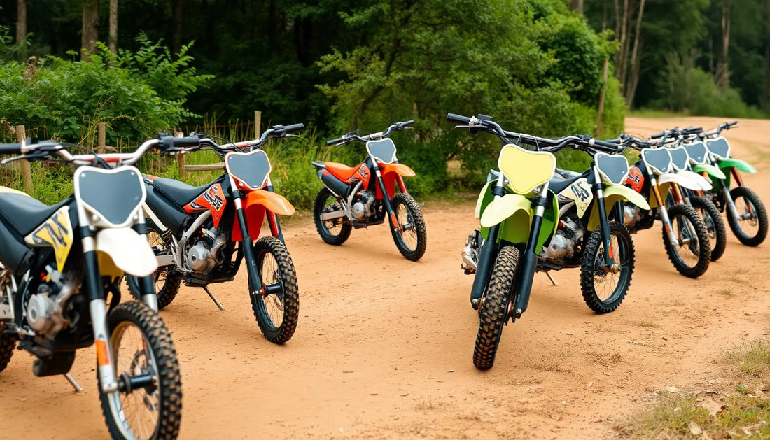 Multiple off-road dirt bikes in various colors parked on a dirt path in a forest setting.