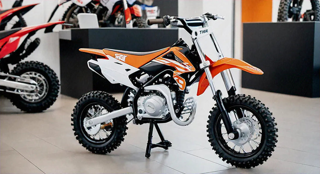 Mini orange and white dirt bike with knobby tires displayed in a showroom setting.