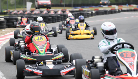 Go-kart racers in helmets driving on an outdoor track during a karting competition