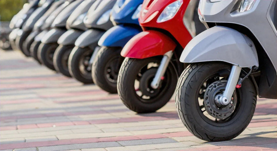 Row of colorful scooters parked on pavement, close-up of front wheels and fenders