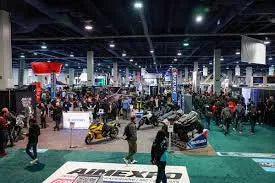 Large indoor expo with people viewing ATVs, dirt bikes, and scooters at a powersports event