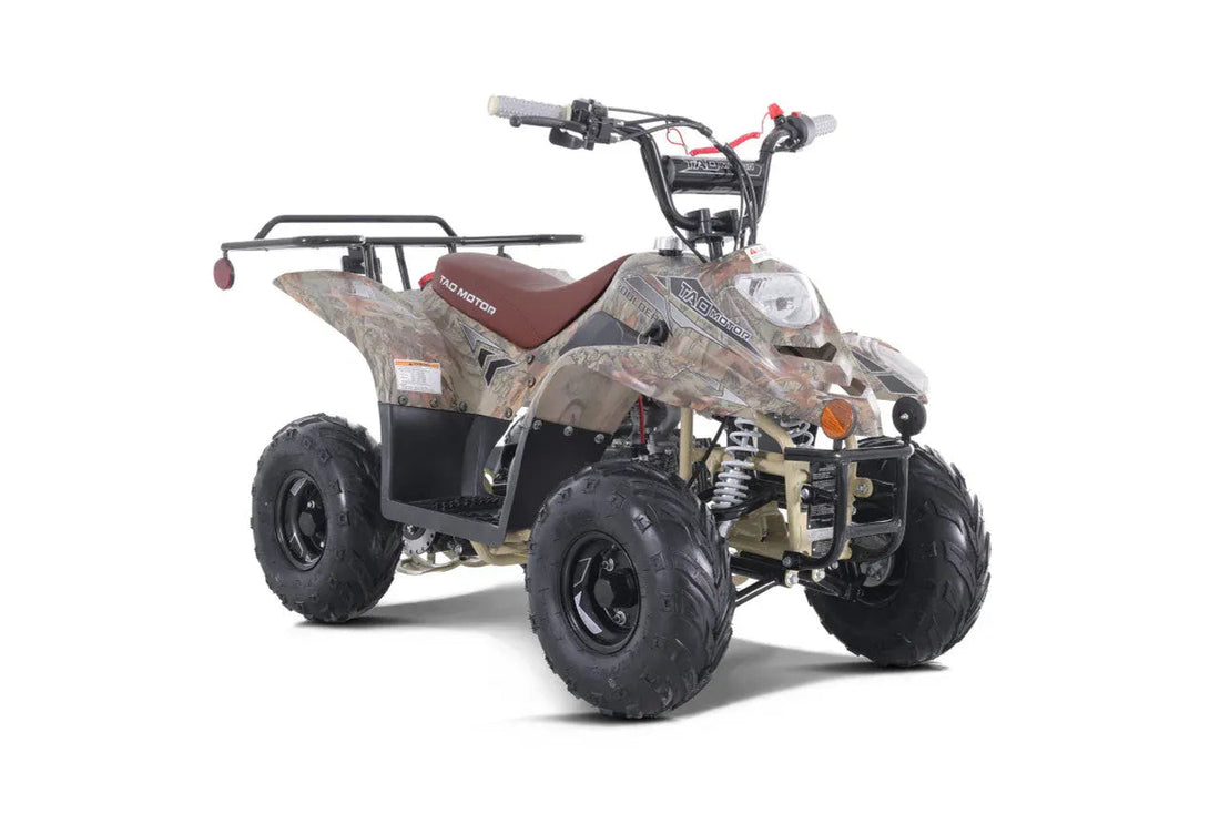 Camo youth ATV with rugged tires, front headlight, and rear cargo rack on white background