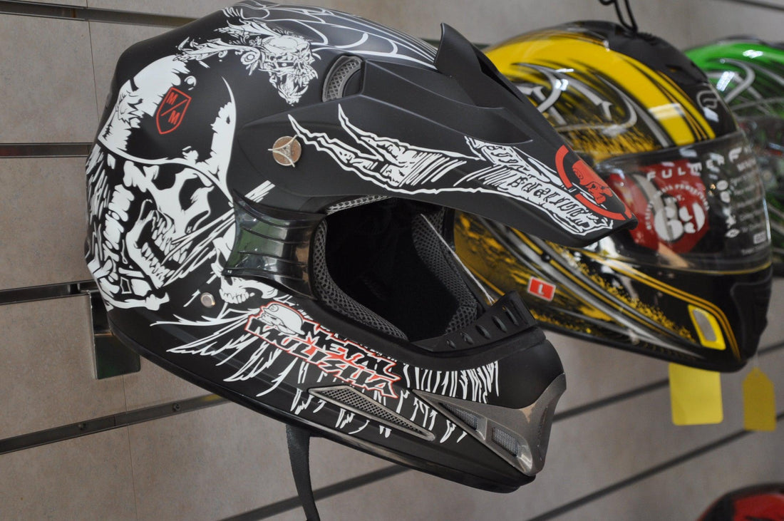 Black motocross helmet with white skull graphics and vents, displayed on store wall