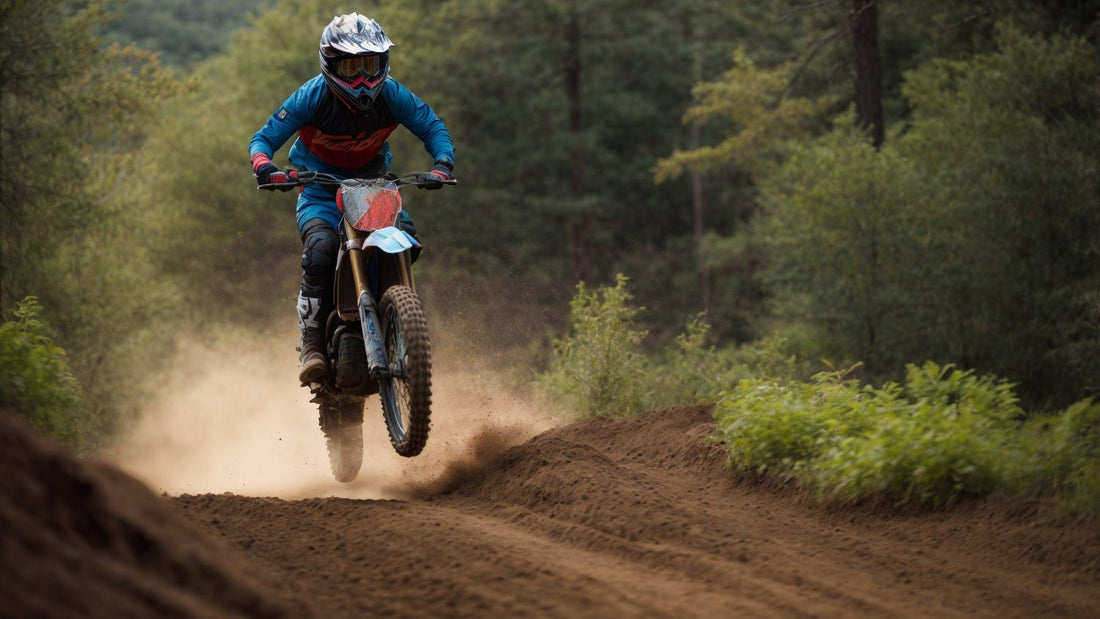 Person riding a dirt bike on a forest trail kicking up dust, wearing helmet and gear