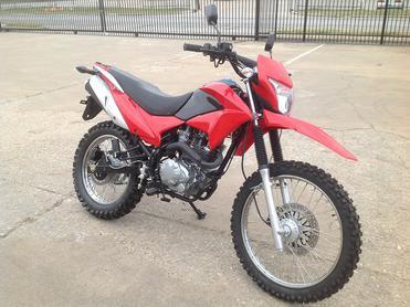 Red off-road dirt bike with knobby tires parked on concrete lot