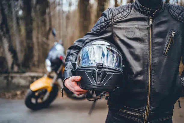 Person in black leather jacket holding motorcycle helmet near yellow dirt bike outdoors