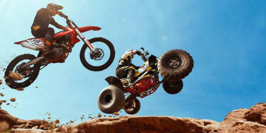 ATV and dirt bike riders jumping on rocky terrain under clear blue sky