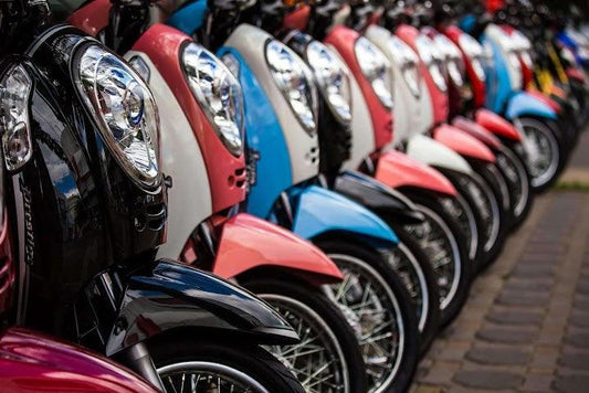 Row of colorful scooters parked outdoors, featuring chrome headlights and spoked wheels