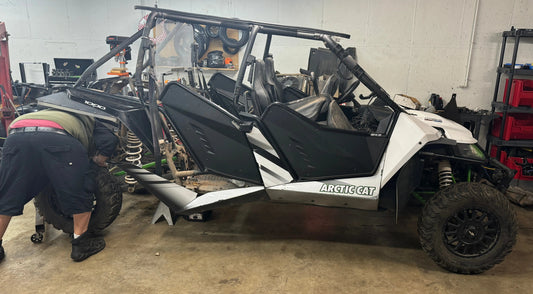 Man repairing white Arctic Cat off-road UTV in a garage workshop setting