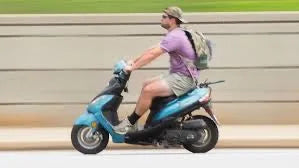 Man riding blue scooter on road, wearing casual clothes and backpack, outdoor setting