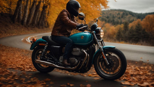 Rider on teal motorcycle on curvy autumn road with fallen leaves and colorful trees