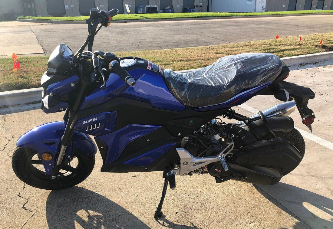 Blue and black youth mini motorcycle with plastic-covered seat parked on concrete near grass and road