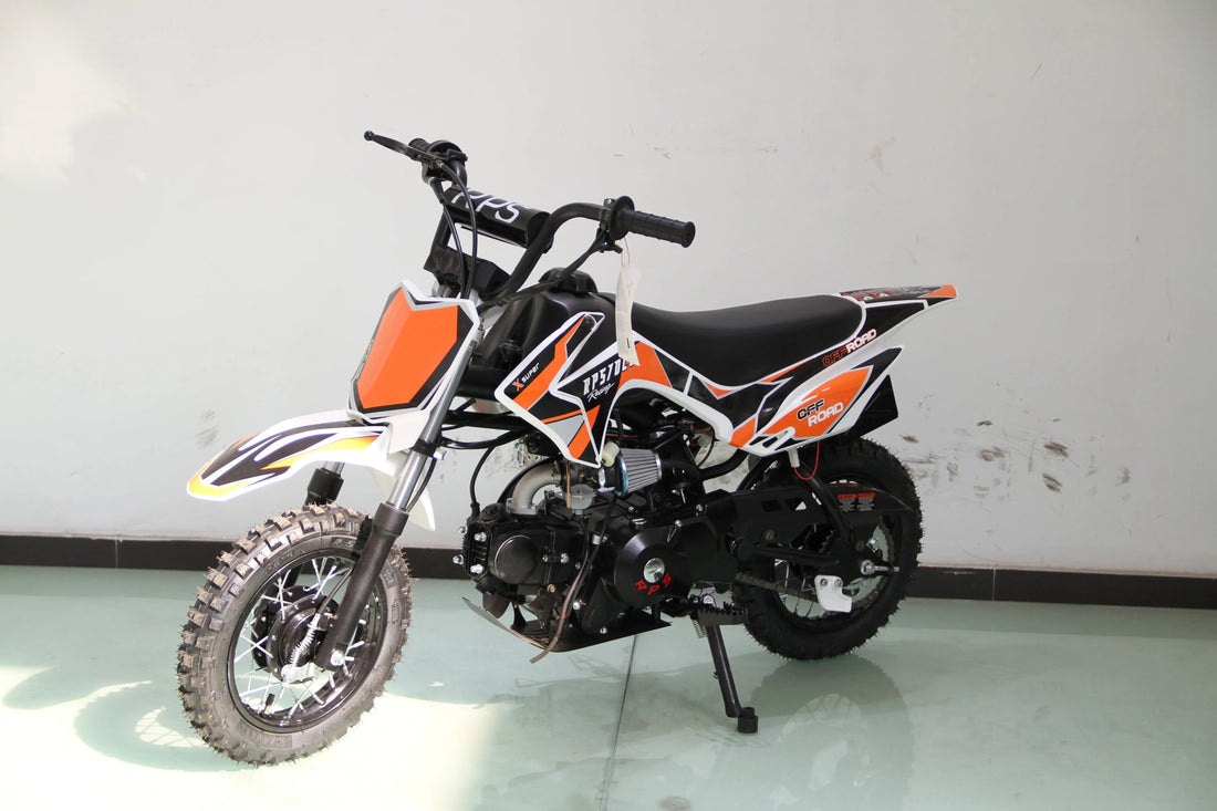 Youth off-road dirt bike with orange, black, and white graphics on a showroom floor