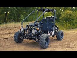 Youth off-road go-kart with roll cage on a dirt trail, rugged tires, and forest background.