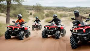 Four riders on youth ATVs driving on a sandy trail in a desert landscape