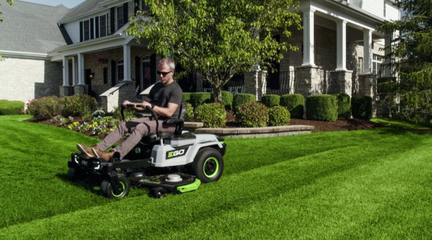 Man using riding lawn mower on green lawn in front of suburban house