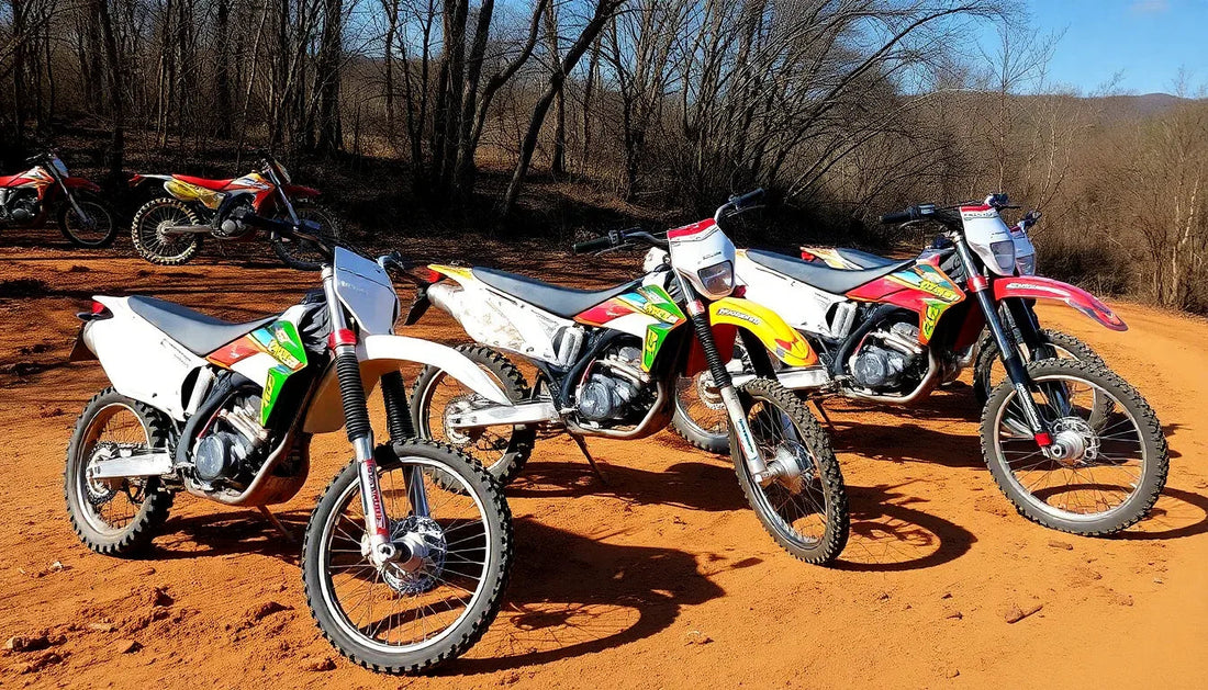 Off-road dirt bikes parked on a sandy trail with bare trees in the background