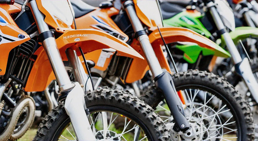 Row of colorful off-road dirt bikes with knobby tires lined up outdoors