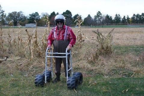 Man outdoors using a walker modified with four all-terrain vehicle wheels on grassy field