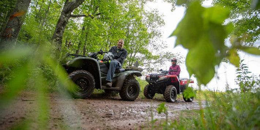 Two people riding ATVs on a forest trail in Wisconsin, surrounded by green trees