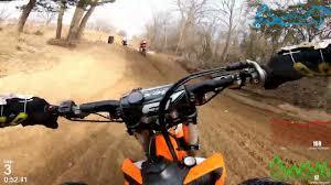 Motocross rider's view on a dirt bike riding a sandy track with trees and racers ahead