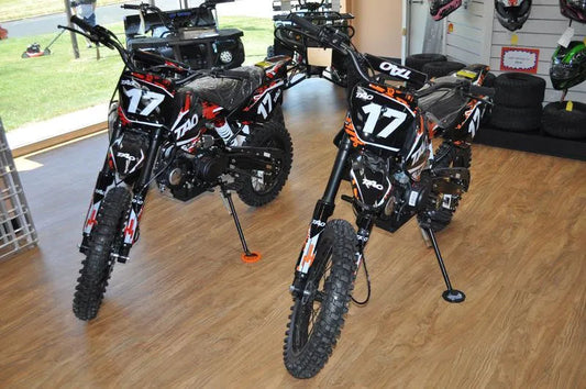 Two black Tao dirt bikes with number 17 decals displayed indoors on wood floor