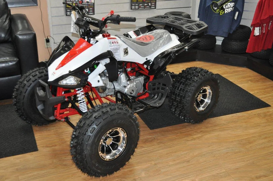 Sport ATV with large off-road tires, red and white body, displayed indoors on a showroom floor
