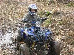Child riding blue ATV in muddy outdoor trail wearing helmet and camo jacket