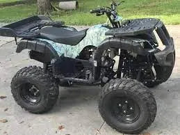 Youth-size camo ATV with rugged tires parked on driveway, outdoor all-terrain vehicle