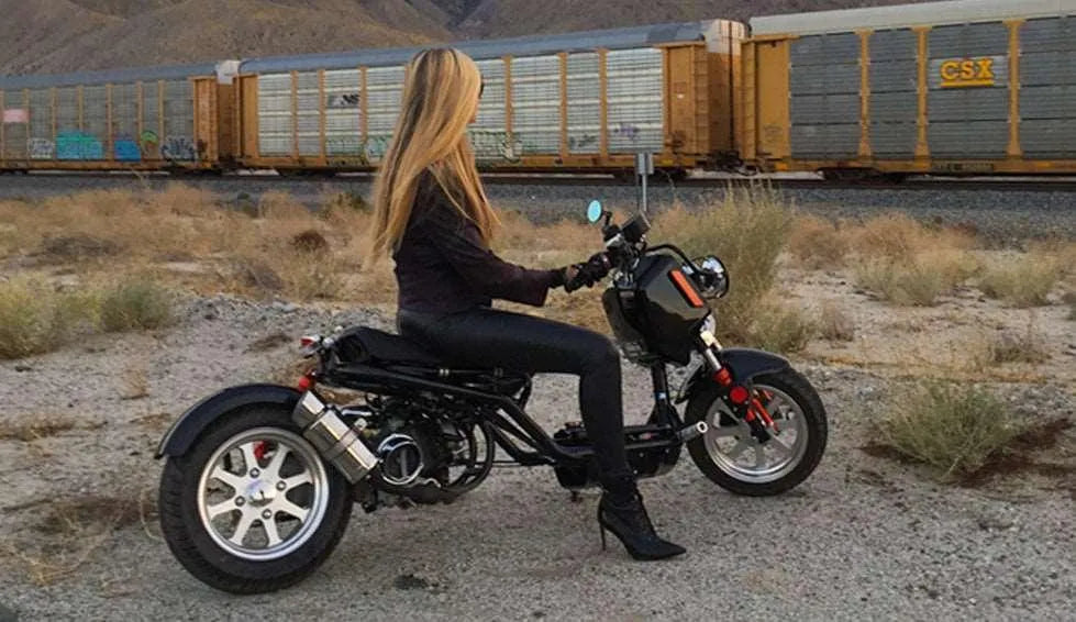 Woman riding mini bike scooter in desert landscape near train, beginner powersports vehicle