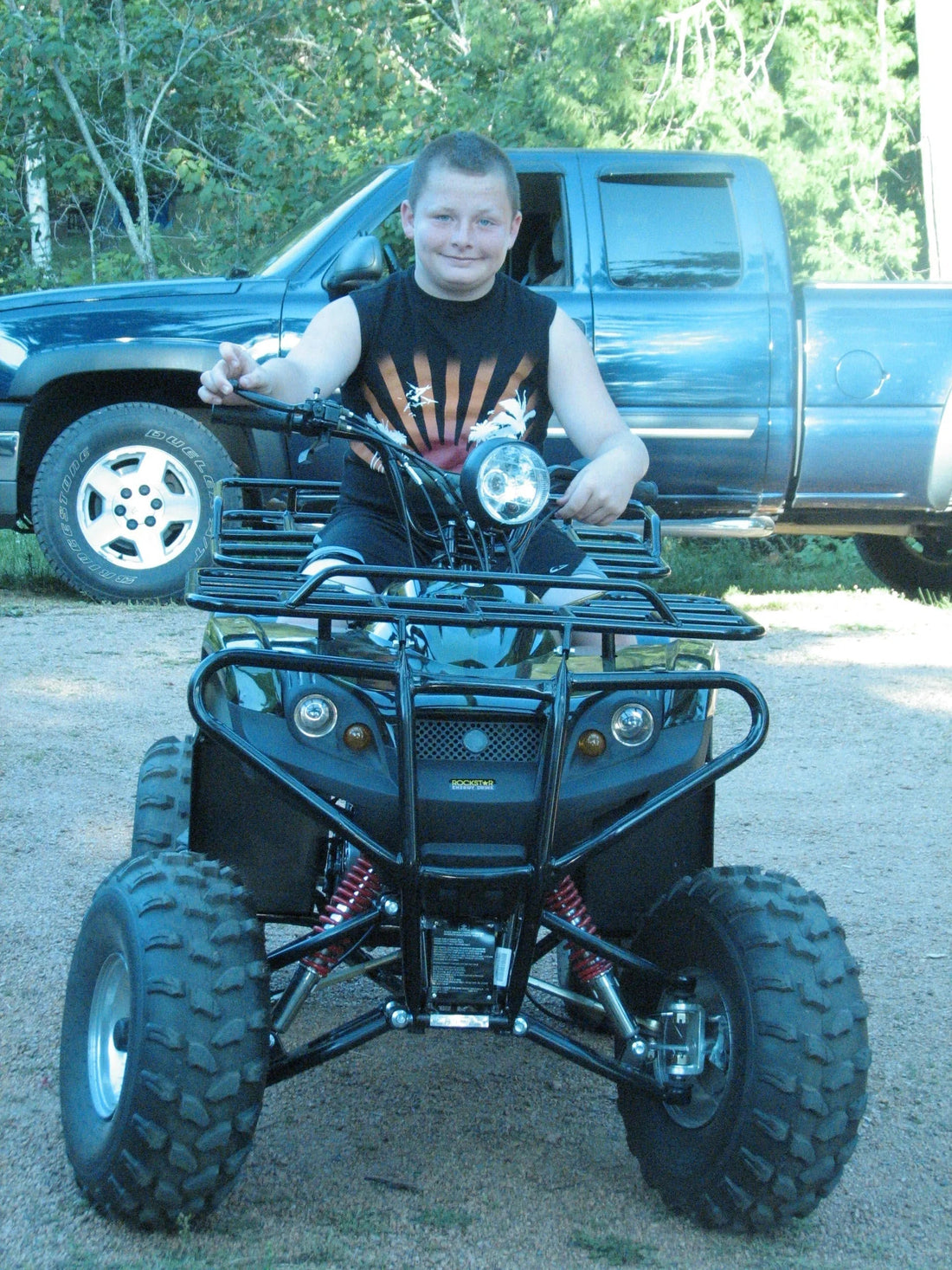 Youth riding all-terrain vehicle ATV outdoors with pickup truck in background