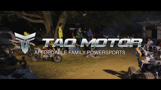 Group of people with dirt bikes, ATVs, and gear outdoors under trees at dusk
