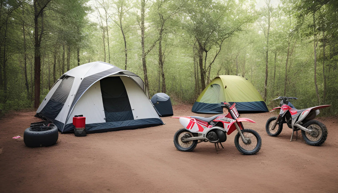 Two off-road dirt bikes parked at a forest campsite with tents on a dirt clearing