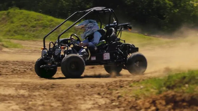 Youth riding a black go-kart on a dirt trail, kicking up dust outdoors