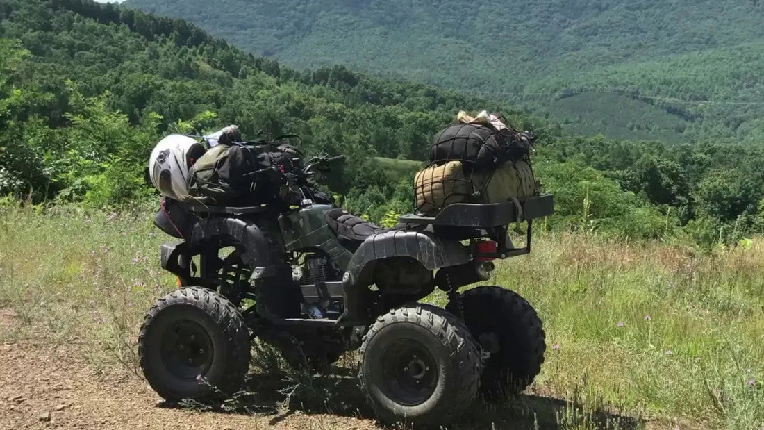 ATV loaded with gear on a grassy trail overlooking forested mountains