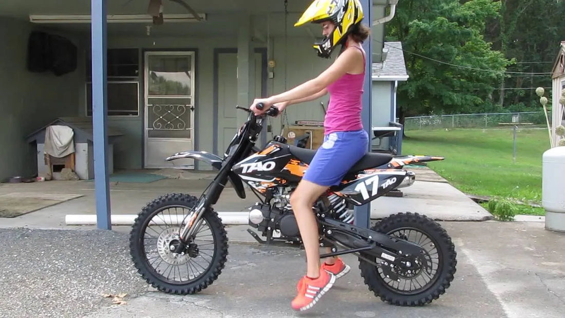 Youth wearing helmet sitting on black and orange Tao dirt bike outdoors on driveway