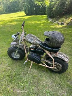 Camo mini bike with matching helmet parked on grass outdoors, off-road motorbike for kids or adults