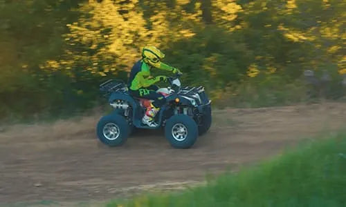 Person riding an ATV quad bike on a dirt trail outdoors, wearing a yellow helmet and gear.