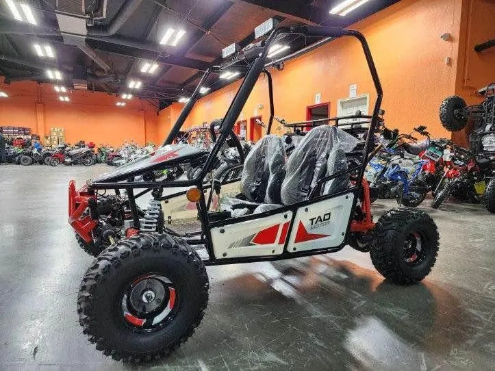 Red and white TAO off-road go-kart with two seats, displayed in a showroom with ATVs and bikes.