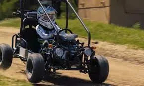 Person driving a go-kart on a dirt track outdoors, wearing helmet and safety gear.