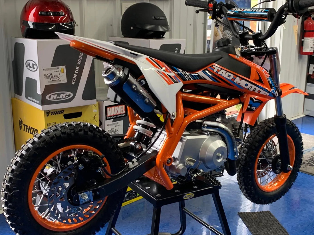 Youth orange Tao Motor dirt bike with knobby tires on showroom display, helmets in background