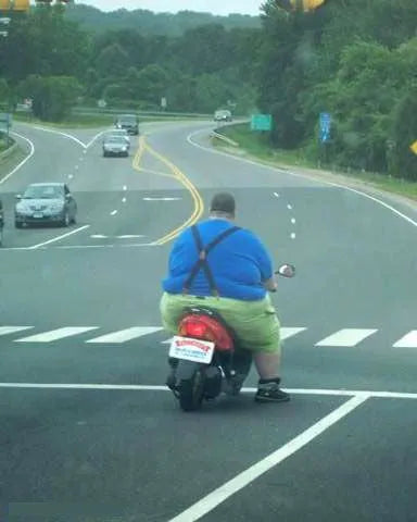 Man riding red scooter on suburban road at intersection, wearing blue shirt and green shorts