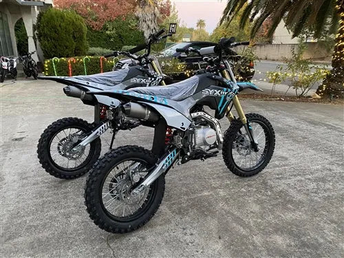 Two SYX Motor dirt bikes parked outdoors on pavement, featuring off-road tires and sporty design.