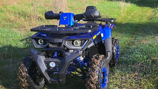 Blue all-terrain ATV with rugged tires and front cargo rack parked on grassy field